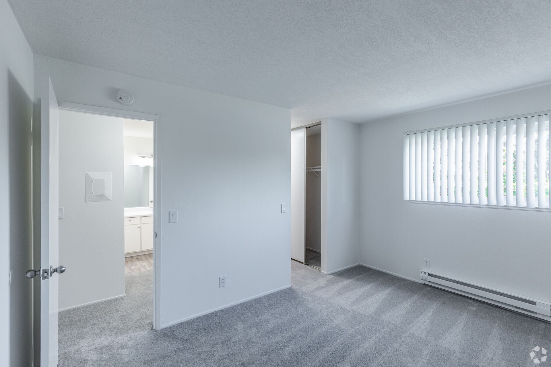 An empty bedroom with a large window and a gray carpet.
