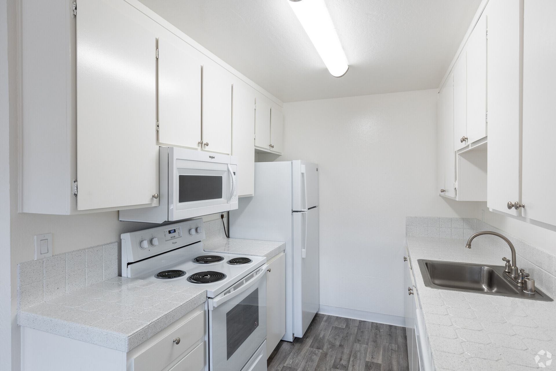 A kitchen with white cabinets , a stove , refrigerator , microwave and sink.