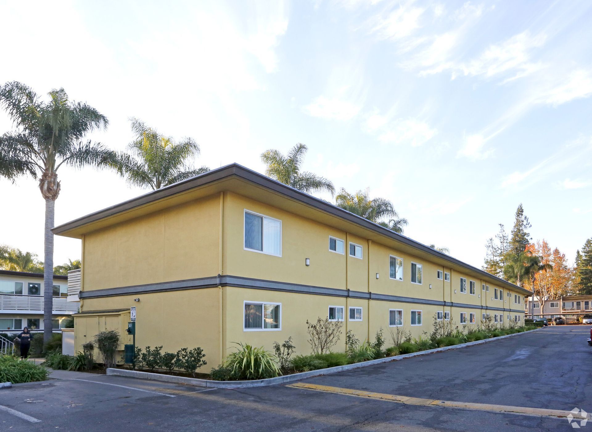 A yellow apartment building with palm trees in front of it