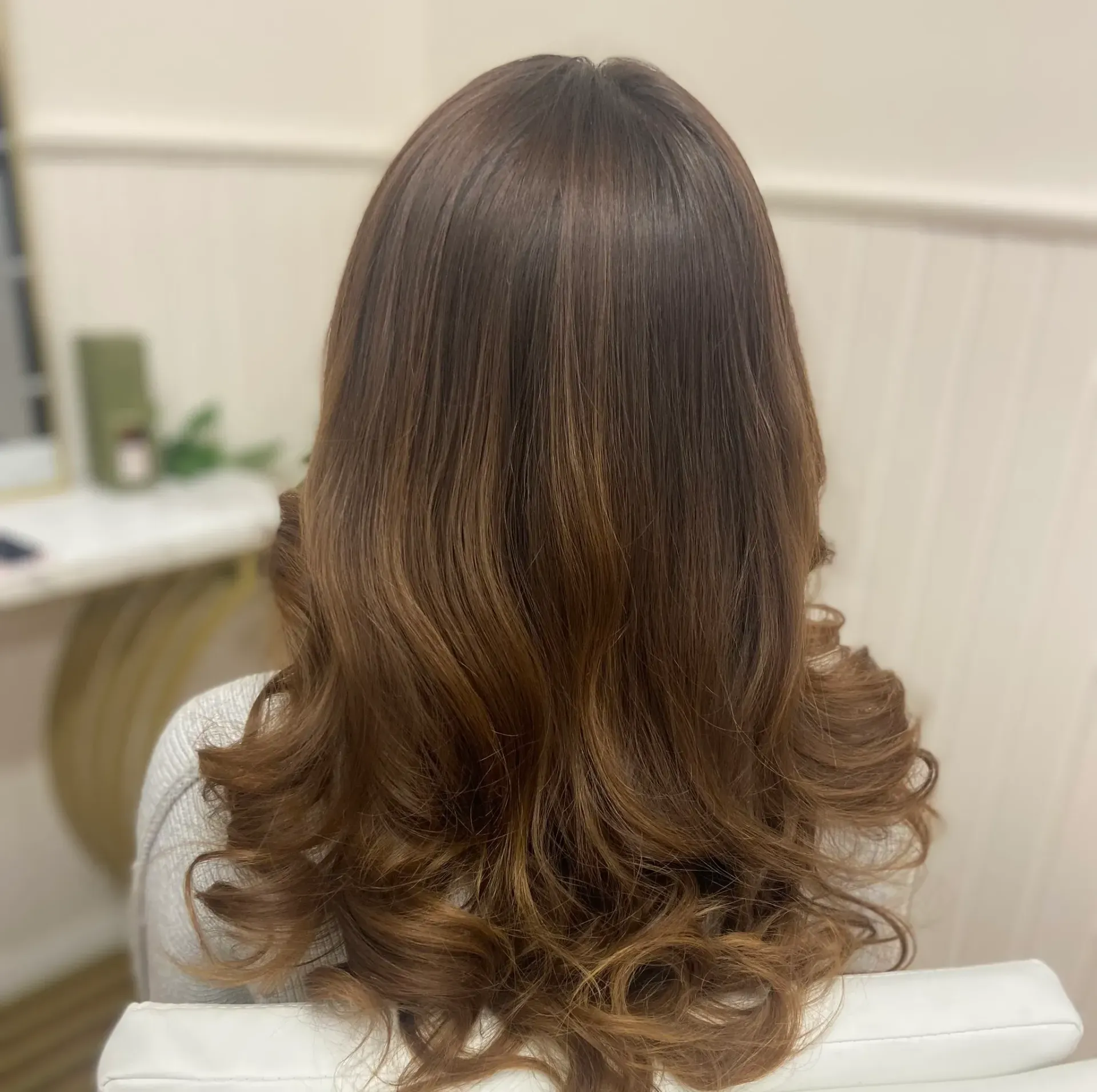 Woman with brown hair, styled with wavy ends. Back view, indoor setting.
