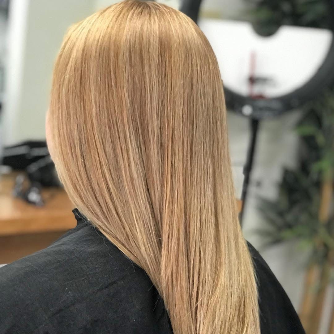 Blonde hair, styled straight, worn by a person facing away, inside a salon.