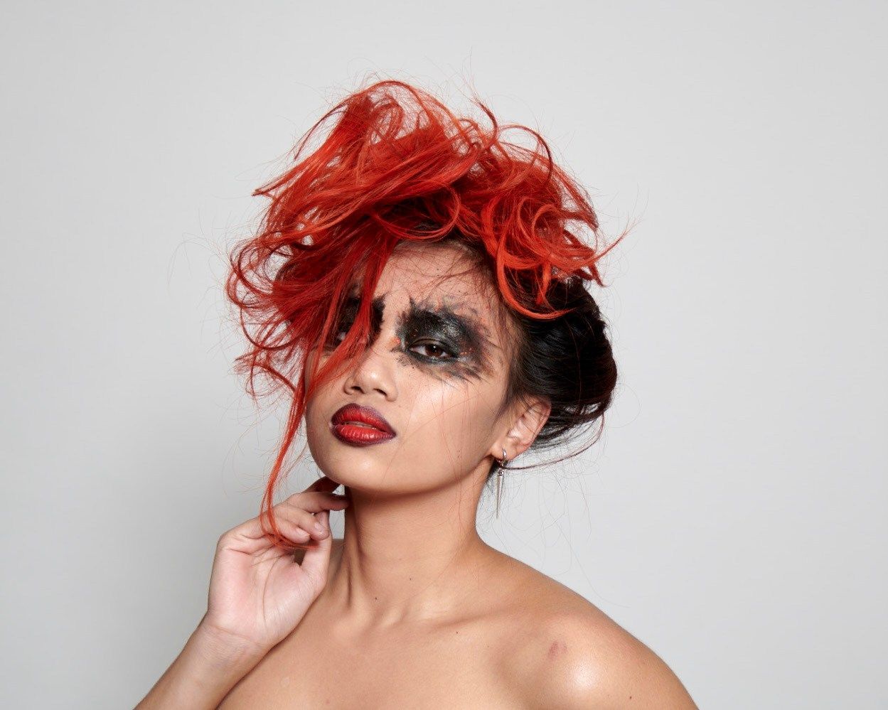 Woman with dramatic red hair and dark eye makeup, red lips, striking pose.