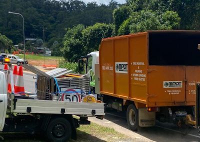 Orange dump truck and white work truck on a road, both with signage; trees in background.