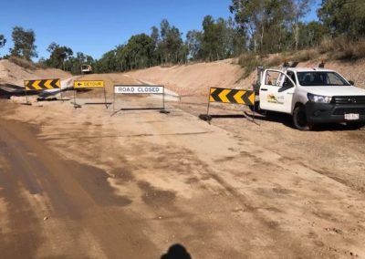 Road closed sign blocks a dirt road, with a white truck parked nearby, under a blue sky.