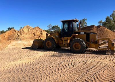 Yellow Caterpillar wheel loader next to dirt piles on a sunny day.
