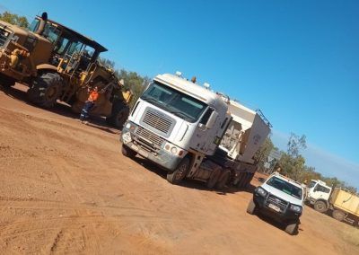 A large white truck and heavy machinery on a dirt road under a clear blue sky.