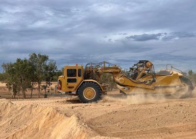 Yellow scraper tractor moving earth on a construction site; overcast sky.