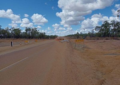 Dirt road with construction ahead, under a blue sky with fluffy clouds.