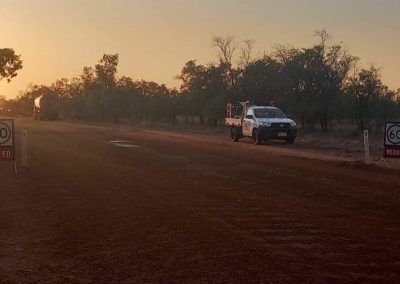 A white truck drives down a dirt road at sunset, passing speed limit signs.