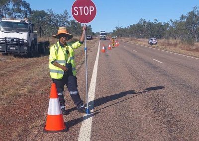 Road worker with a stop sign and safety cone on a highway, directing traffic.
