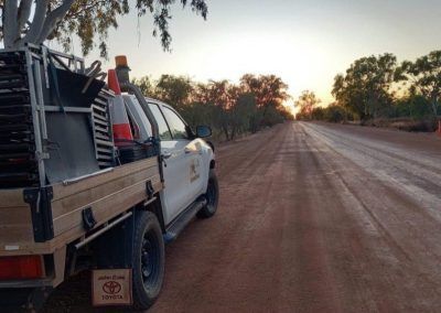 A work truck on a red dirt road with traffic cones. Sunset in the background.