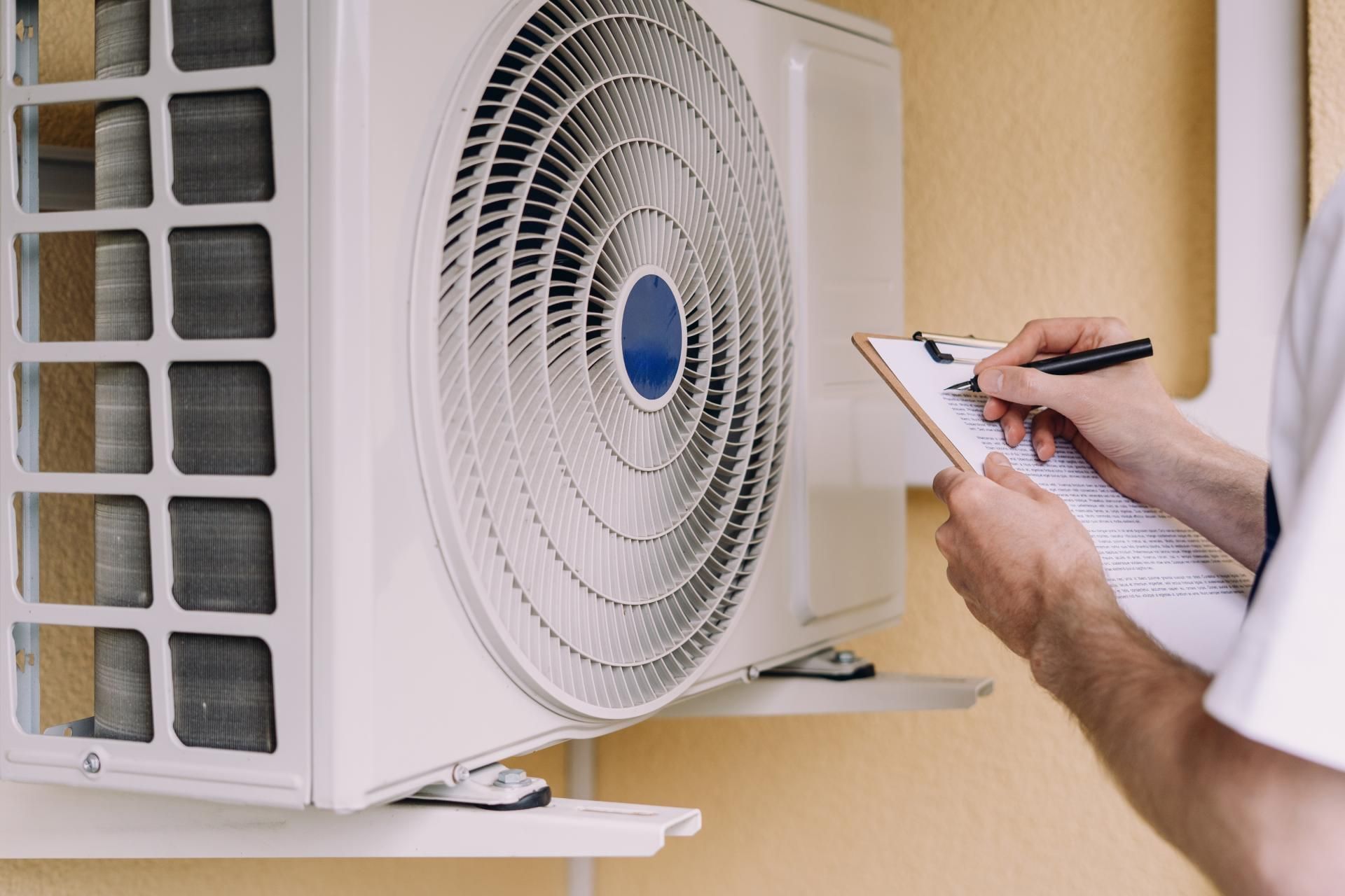 Person inspecting an outdoor air conditioning unit, writing on a clipboard.