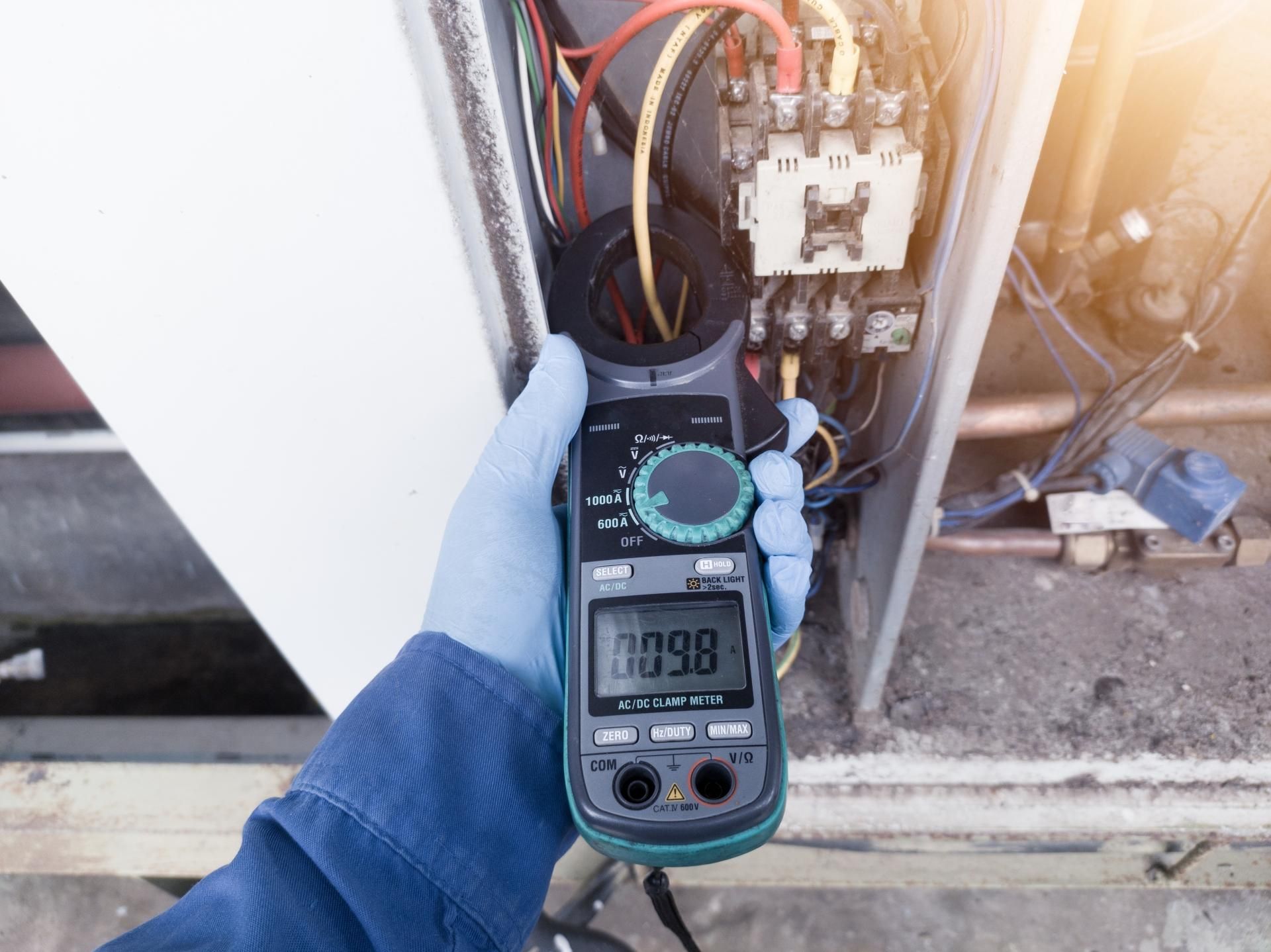 Technician uses a clamp meter to measure electrical current in an HVAC unit.