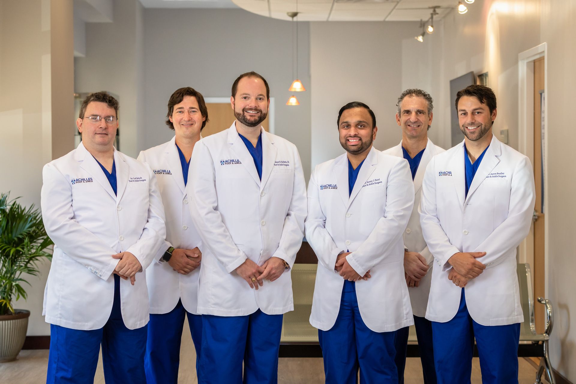 A group of doctors in white coats and blue scrubs pose for a picture