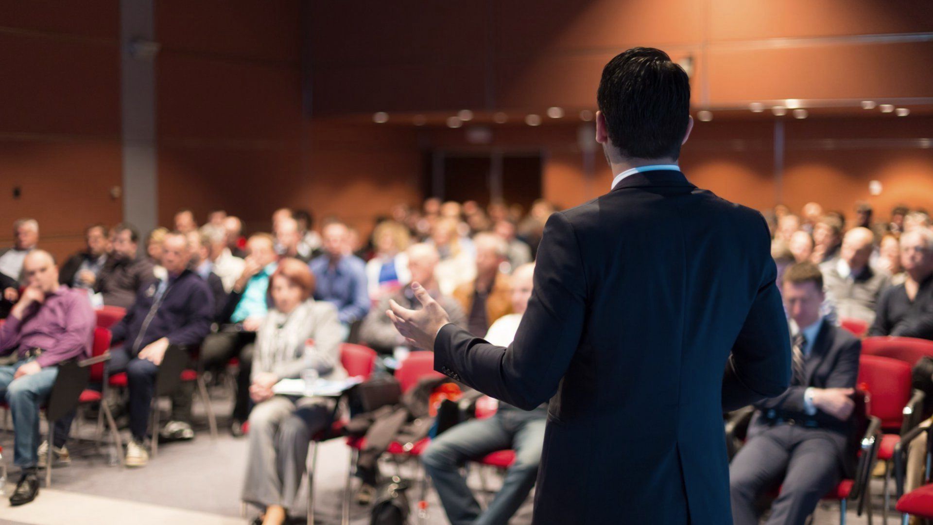 A man in a suit is giving a presentation to a large group of people