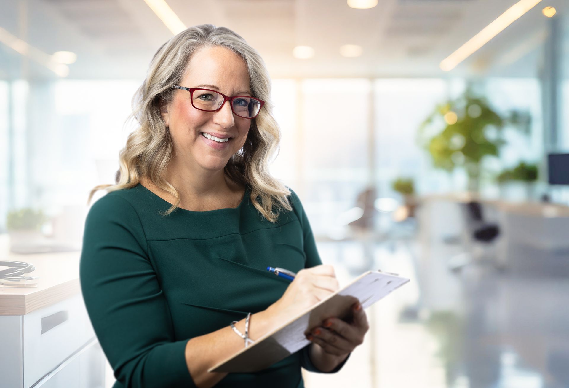 A woman is smiling while holding a clipboard and writing on it.