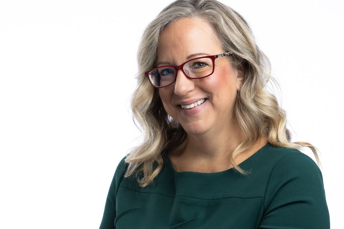 A woman wearing glasses and a green shirt is smiling for the camera.