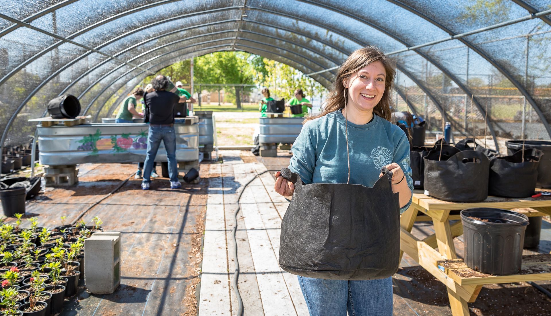 A woman is holding a black bag in a greenhouse