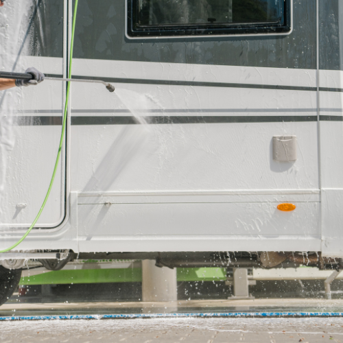 Person power washing a white and gray recreational vehicle.