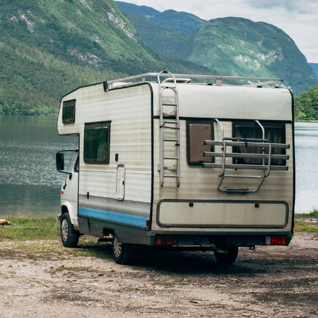 White RV parked on a lake shore with mountains in the background.