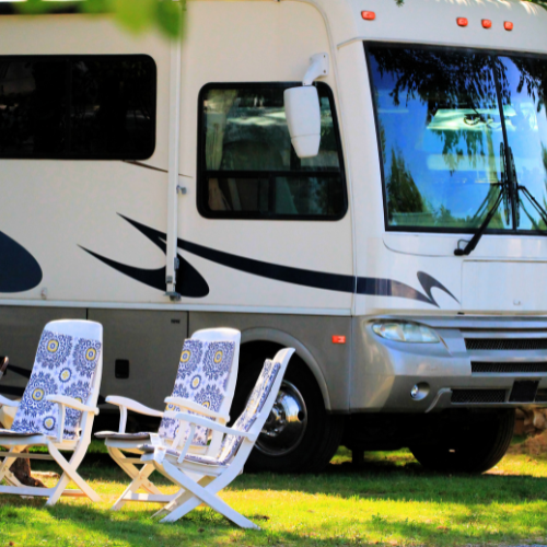 RV parked on grass with two white chairs with blue and yellow patterned seats.