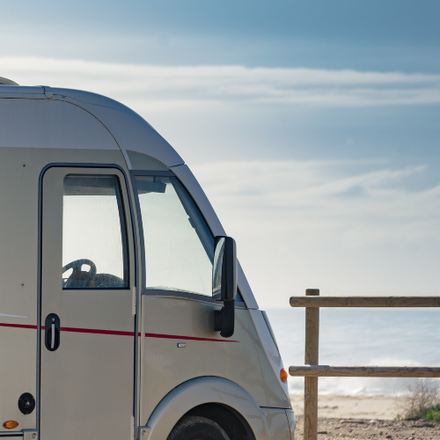 RV parked on a beach with the ocean and a wooden fence in the background.