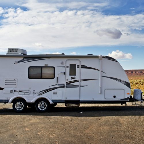 White travel trailer parked on asphalt under a cloudy sky, with desert landscape in background.