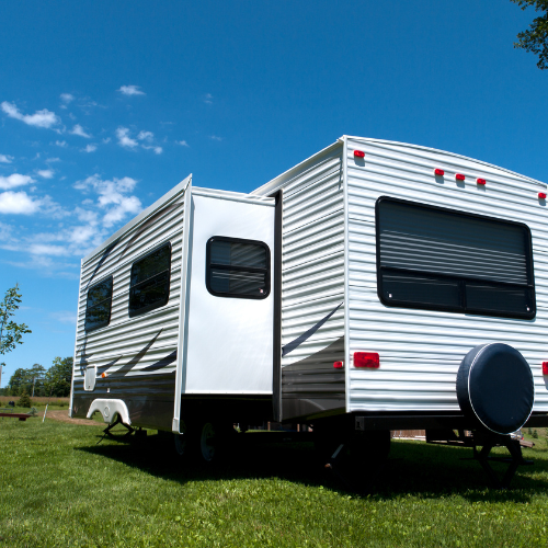 White camper trailer on green grass, with the door open, under a blue sky.