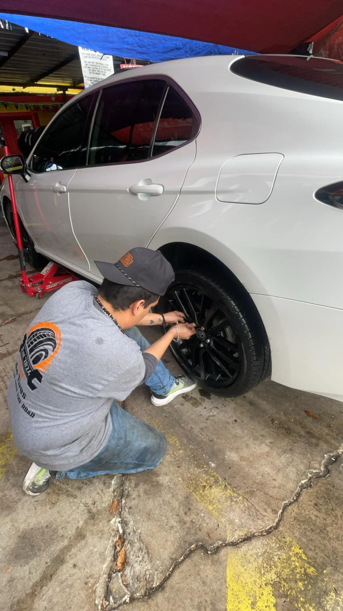 Mechanic changing a black tire on a white car; kneeling, working outside.