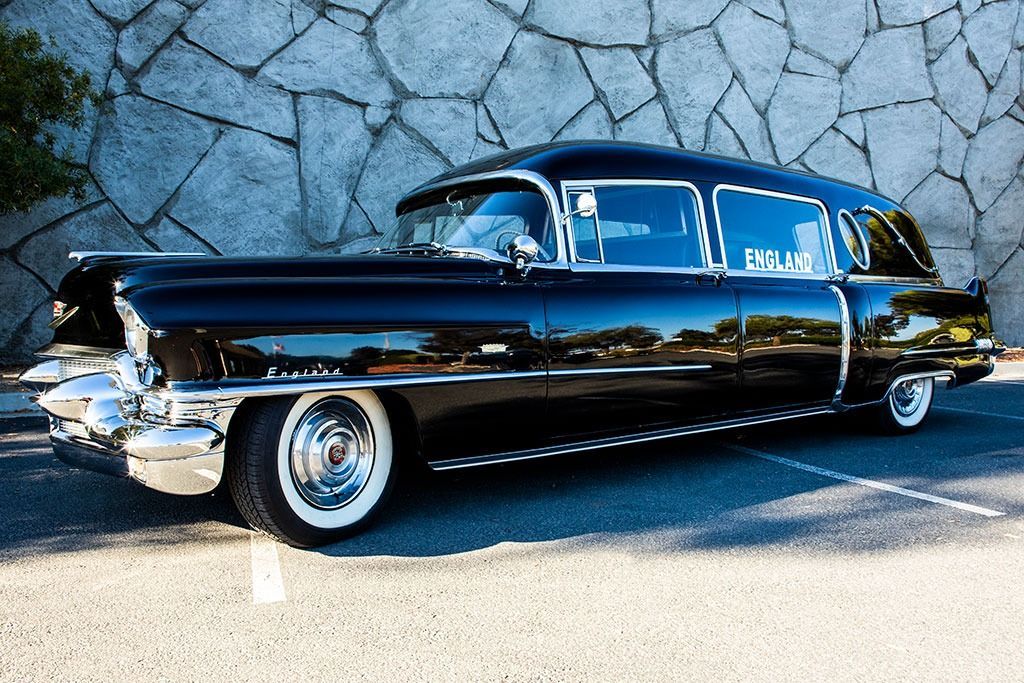 Black vintage hearse parked in front of a stone wall.