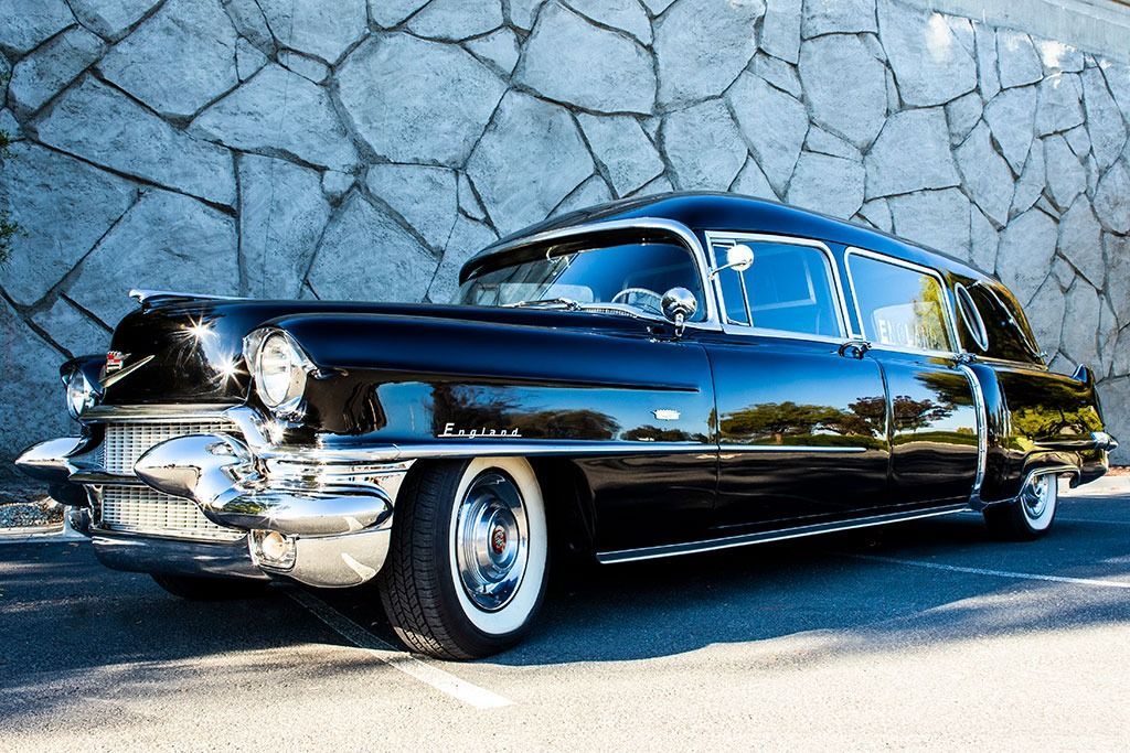 Black vintage hearse with chrome accents parked against a stone wall.