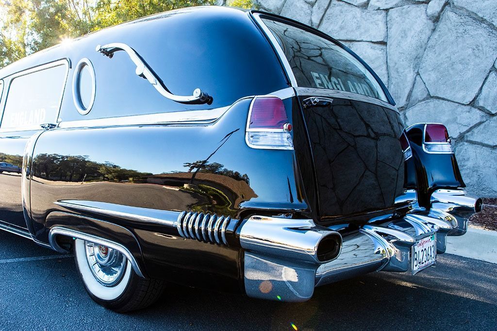 Black classic hearse with chrome accents parked, reflecting light.