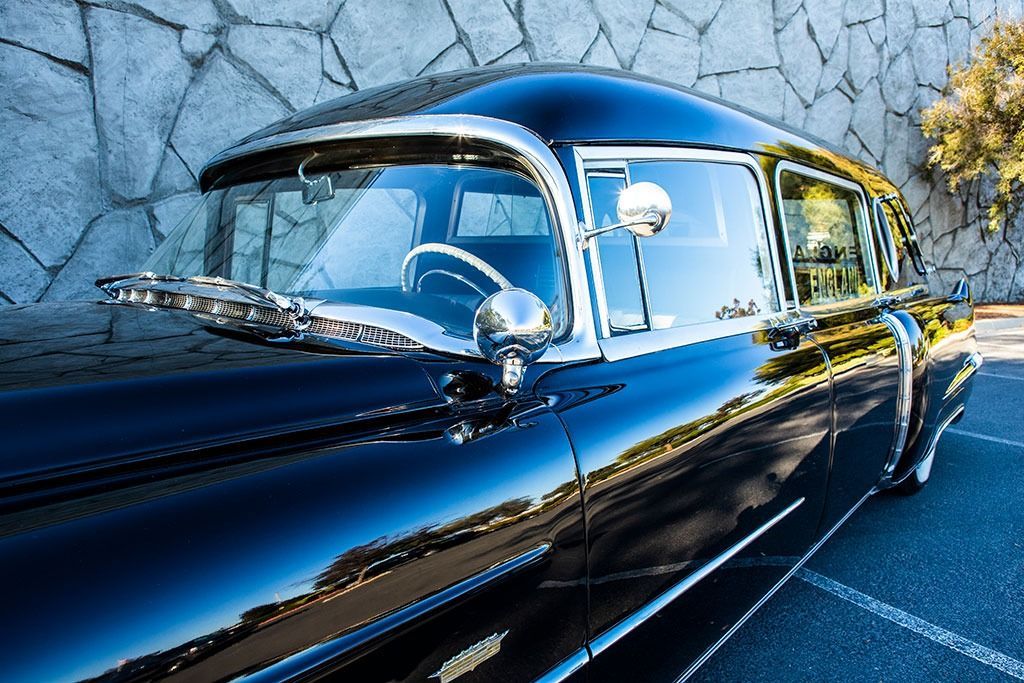 Black classic car parked in front of a stone wall; chrome details reflect sunlight.