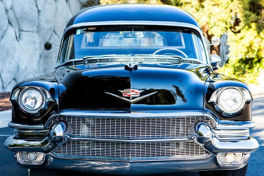 Black classic Cadillac car with chrome grill, headlights, and side mirrors parked outdoors.