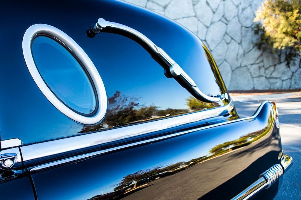 Black classic car's rear section with chrome accents, oval window, and reflections of surroundings.