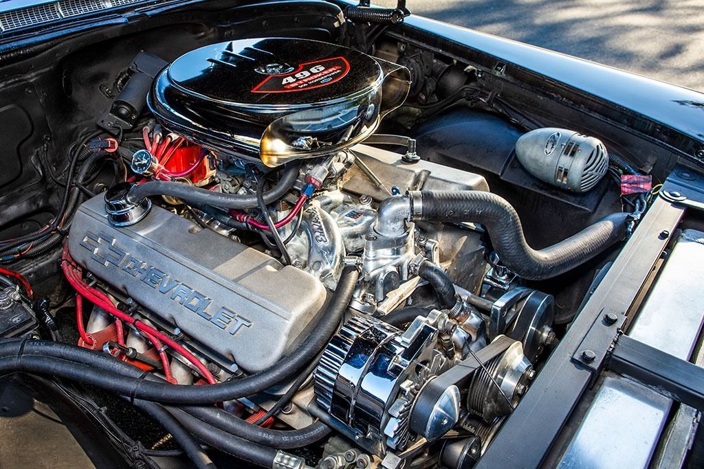 Shiny black classic car engine bay, chrome parts, silver engine cover, black air filter.