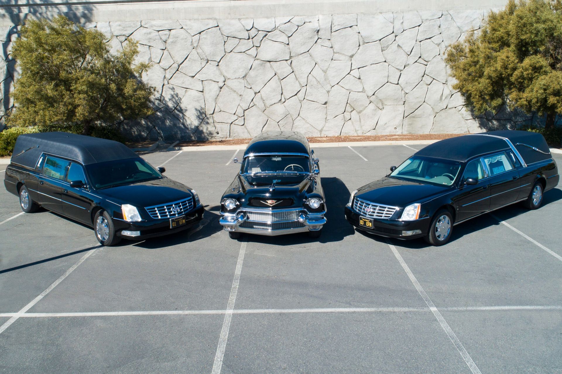 Three black hearses parked in a lot, with a classic car hearse in the center.