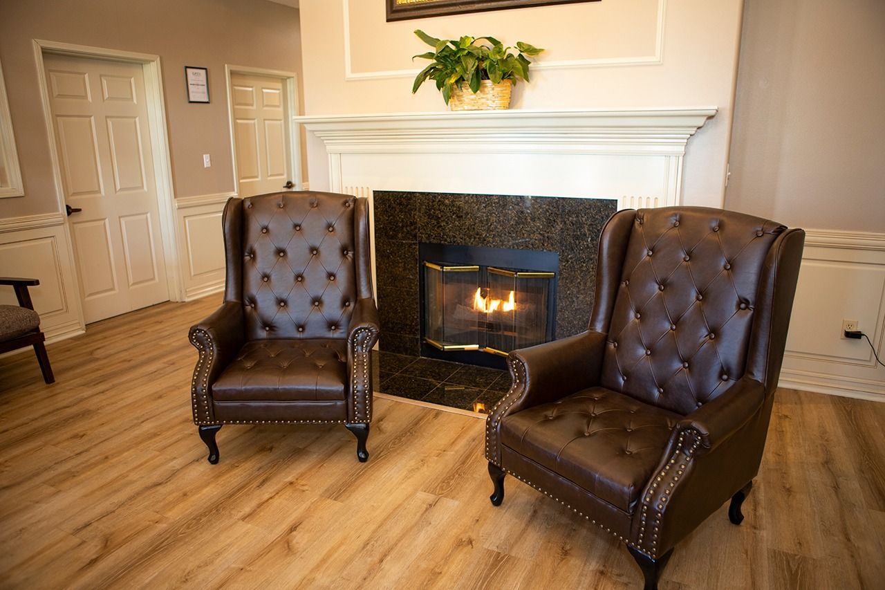 Two brown leather wingback chairs face a fireplace in a sitting area.