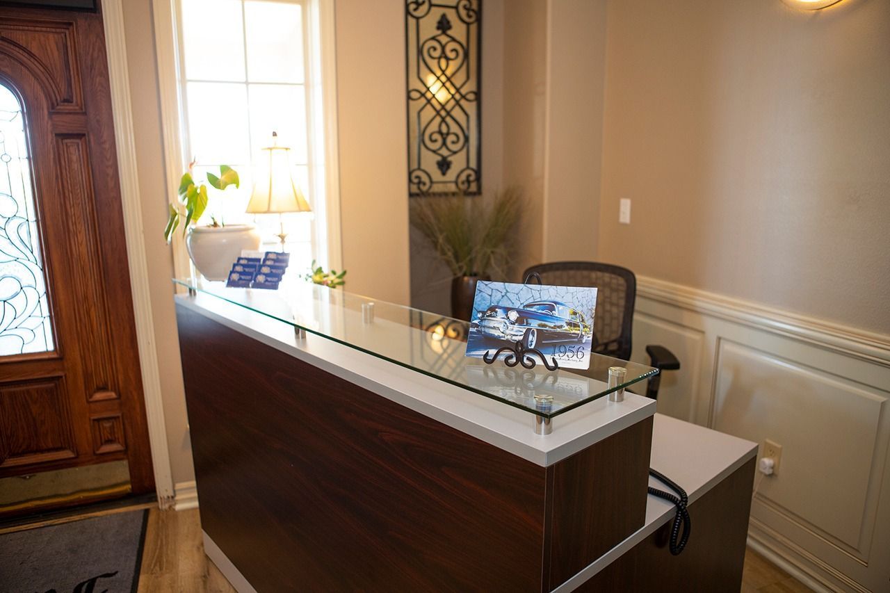 Reception desk in a well-lit entryway; wood and glass, framed art, decorative lighting.