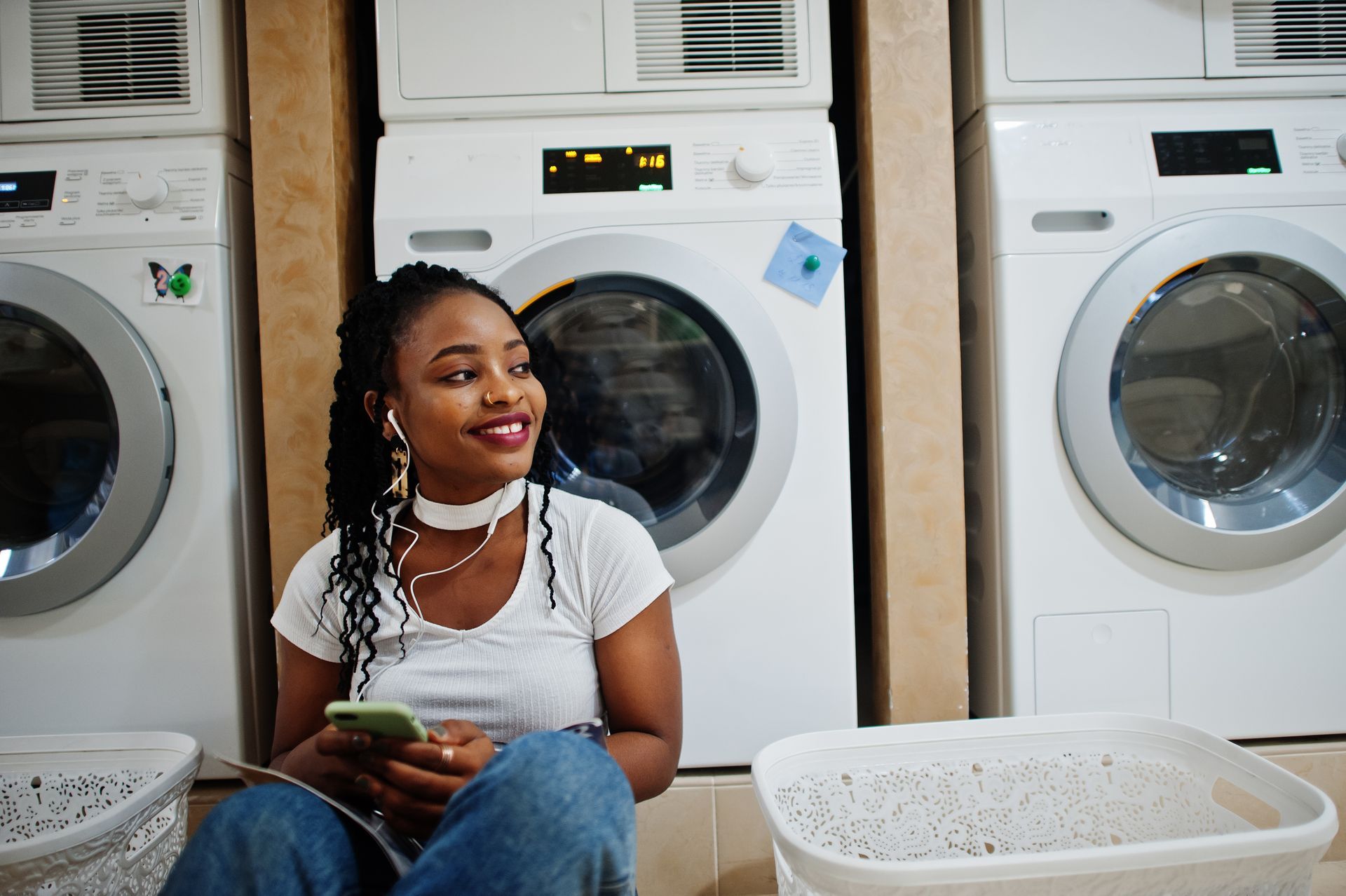 Woman sitting in a laundromat, smiling while holding a phone beside washing machines Woman sitting in a laundromat, smiling while holding a phone beside washing machines