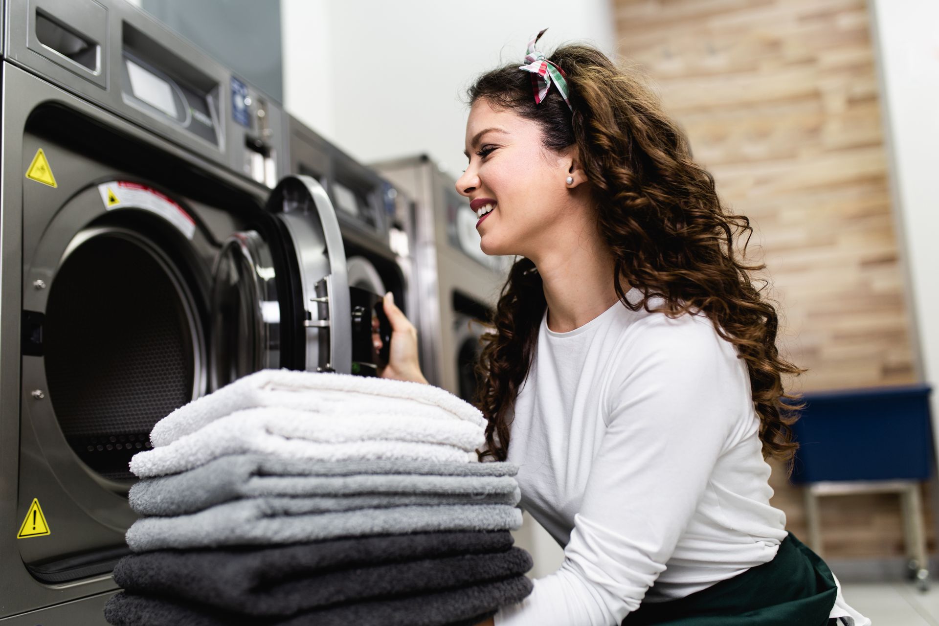 Woman loading laundry into a washing machine in a laundromat, beside a stack of folded towels. Woman loading laundry into a washing machine in a laundromat, beside a stack of folded towels.