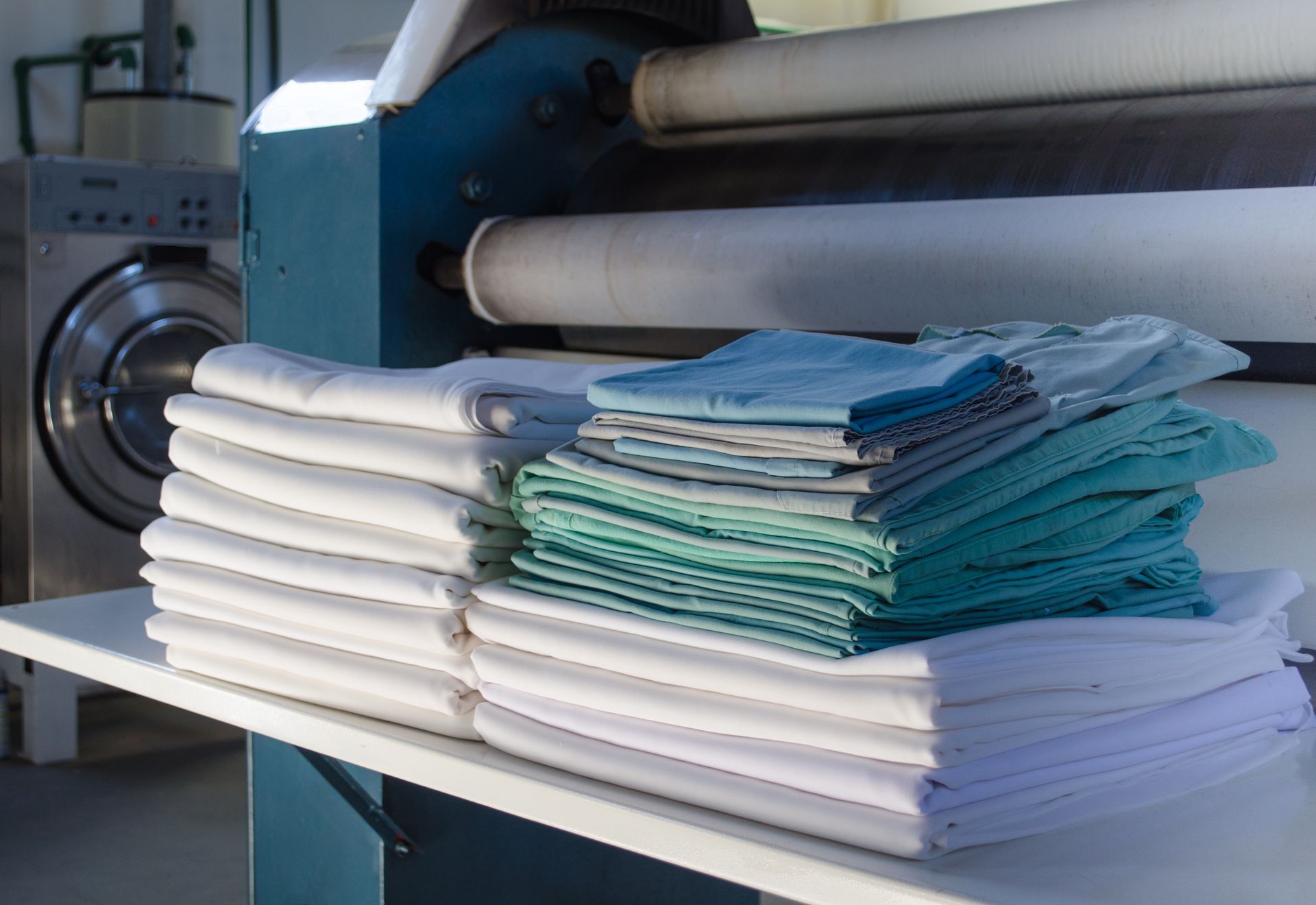 Stainless steel machine folding neatly stacked white, blue, and green towels in a laundry facility Stainless steel machine folding neatly stacked white, blue, and green towels in a laundry facility