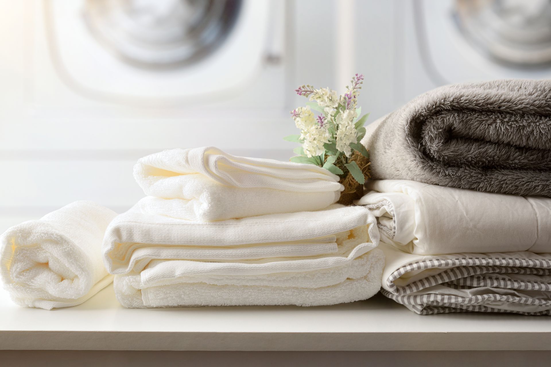 Stacked white towels and folded gray towels on a bathroom shelf with a small flower arrangement Stacked white towels and folded gray towels on a bathroom shelf with a small flower arrangement