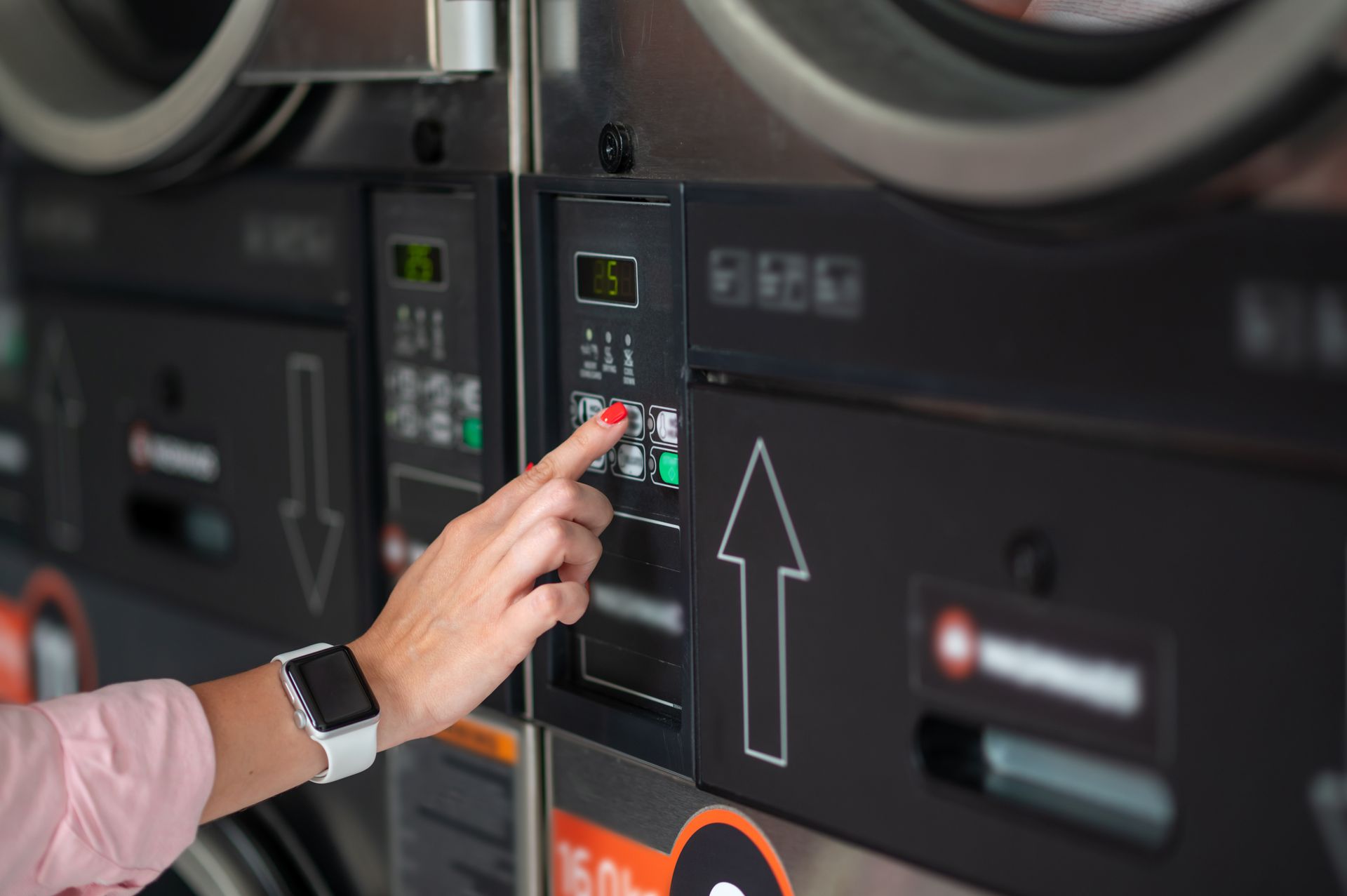 Hand pressing buttons on a laundromat washing machine control panel with an upward arrow Hand pressing buttons on a laundromat washing machine control panel with an upward arrow