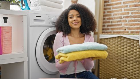 Woman holding folded towels in a laundry room beside a washing machine