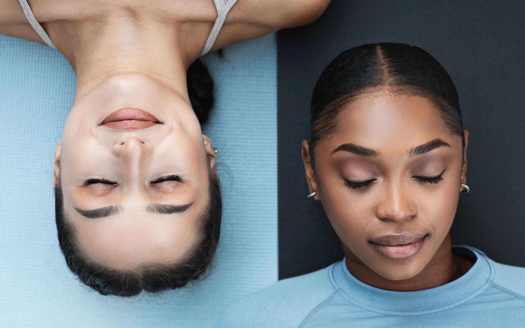 Two women are laying on a yoga mat with their eyes closed.