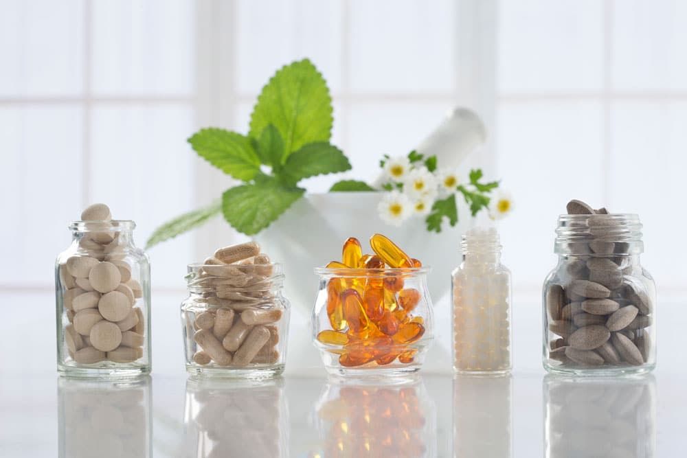 There are many different types of pills in jars on the table.