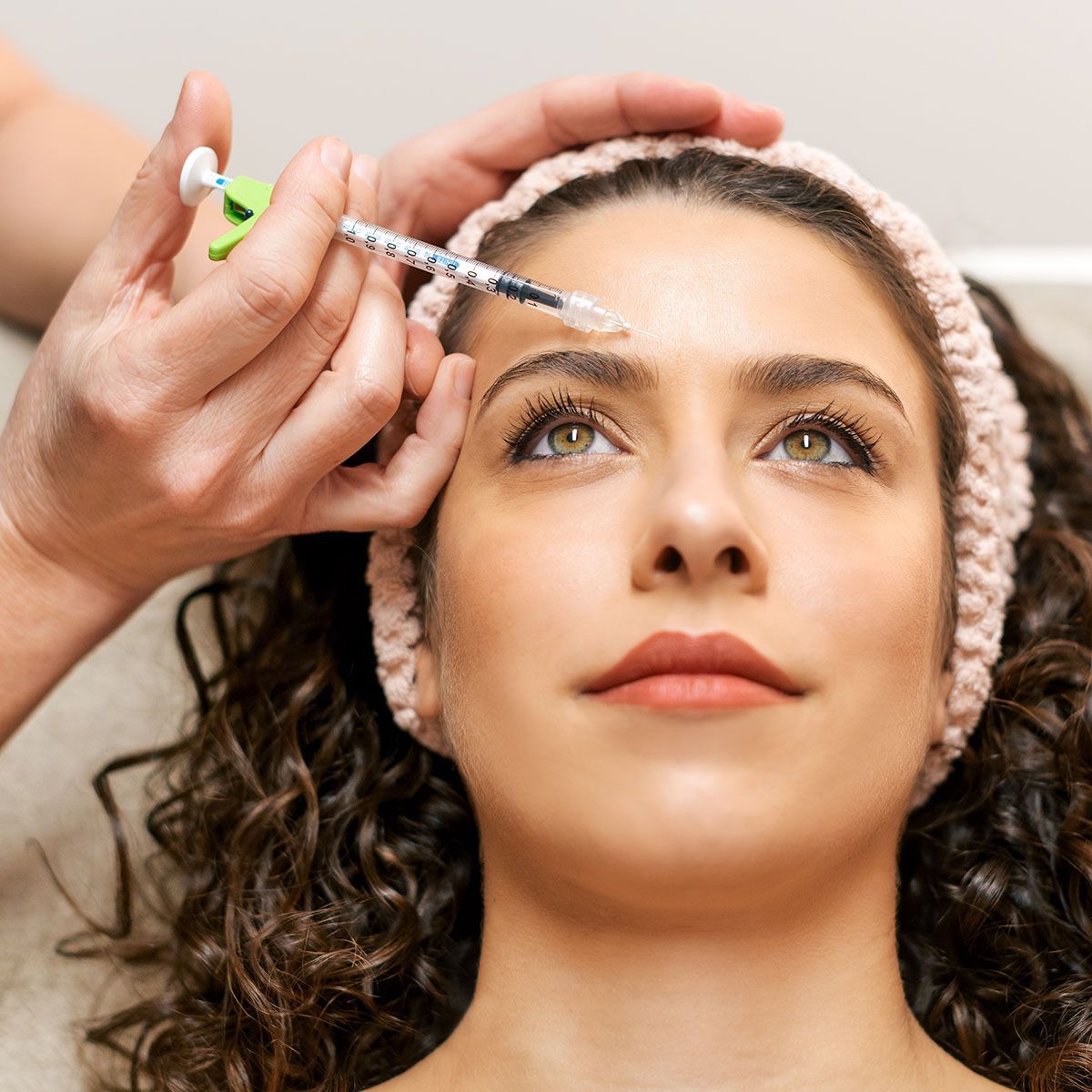 A woman is getting a botox injection on her forehead