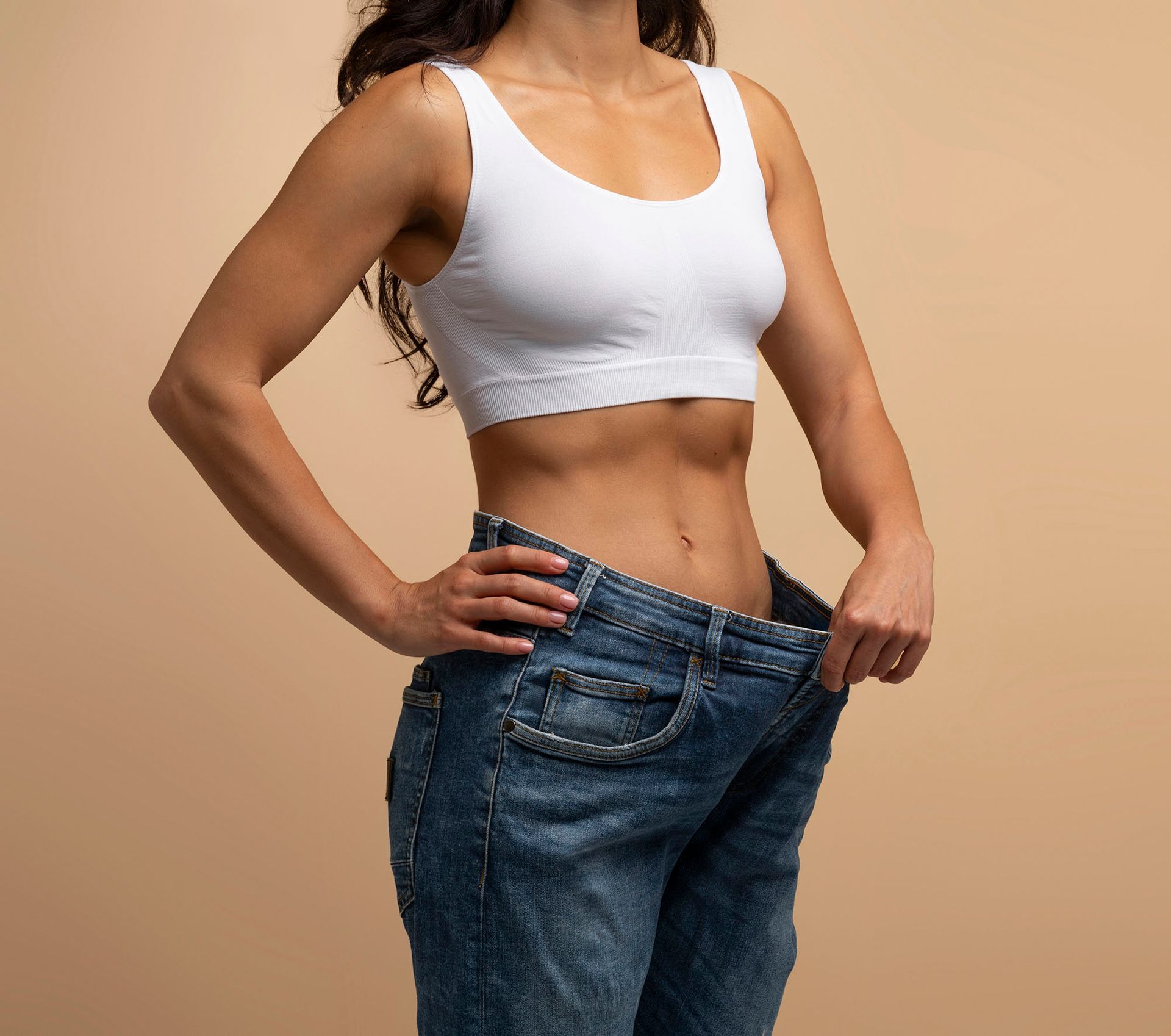 A woman in a white crop top and jeans is standing with her hands on her hips.