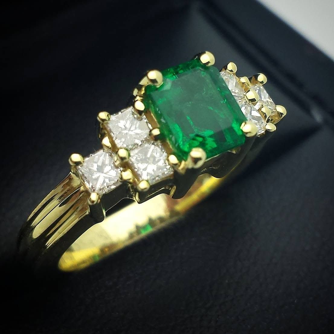 Gold ring with a large emerald-cut green gemstone and small clear stones on a black background